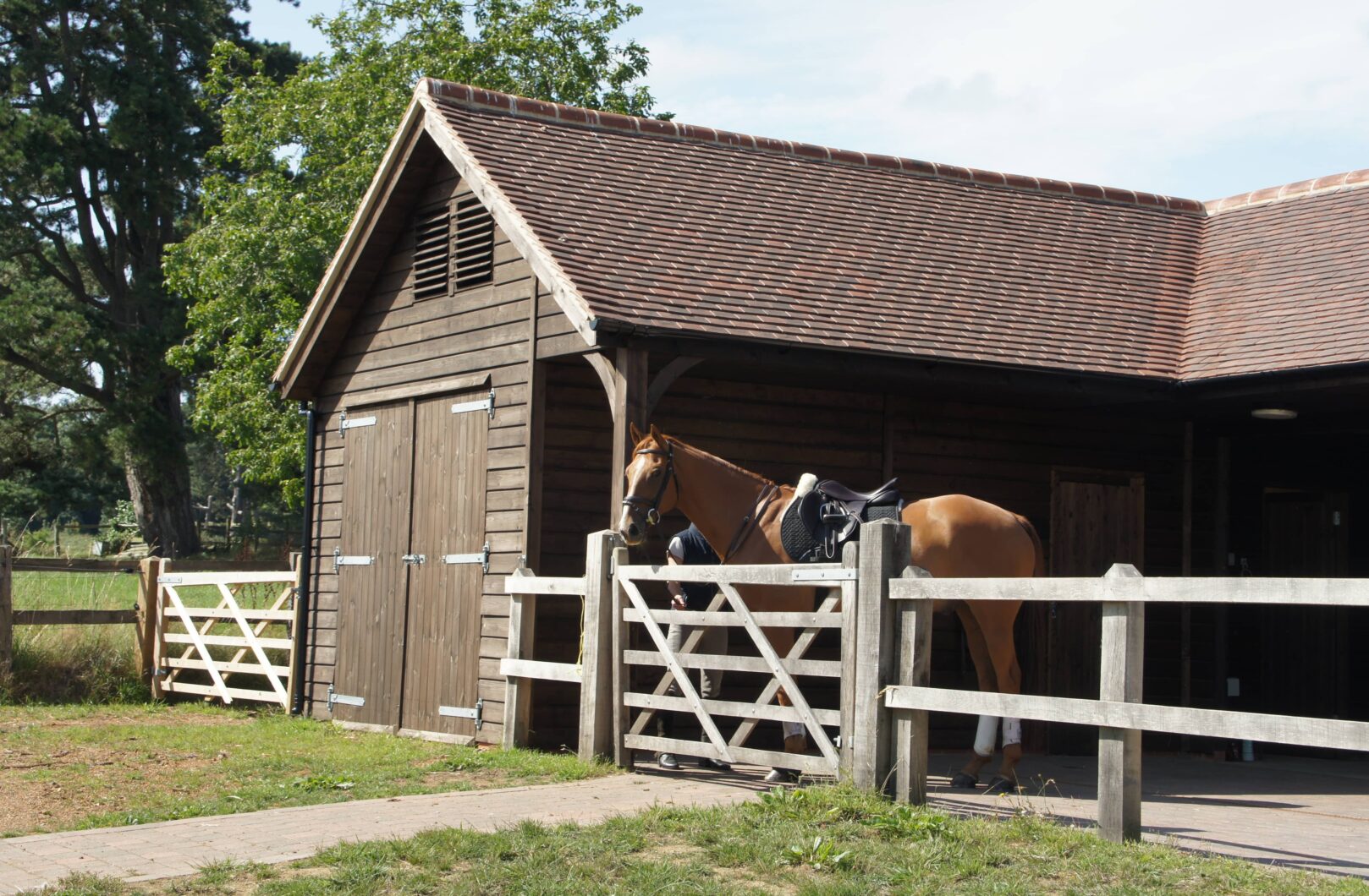Brown L-shape stable block with clay tiles with horse in yard out the front
