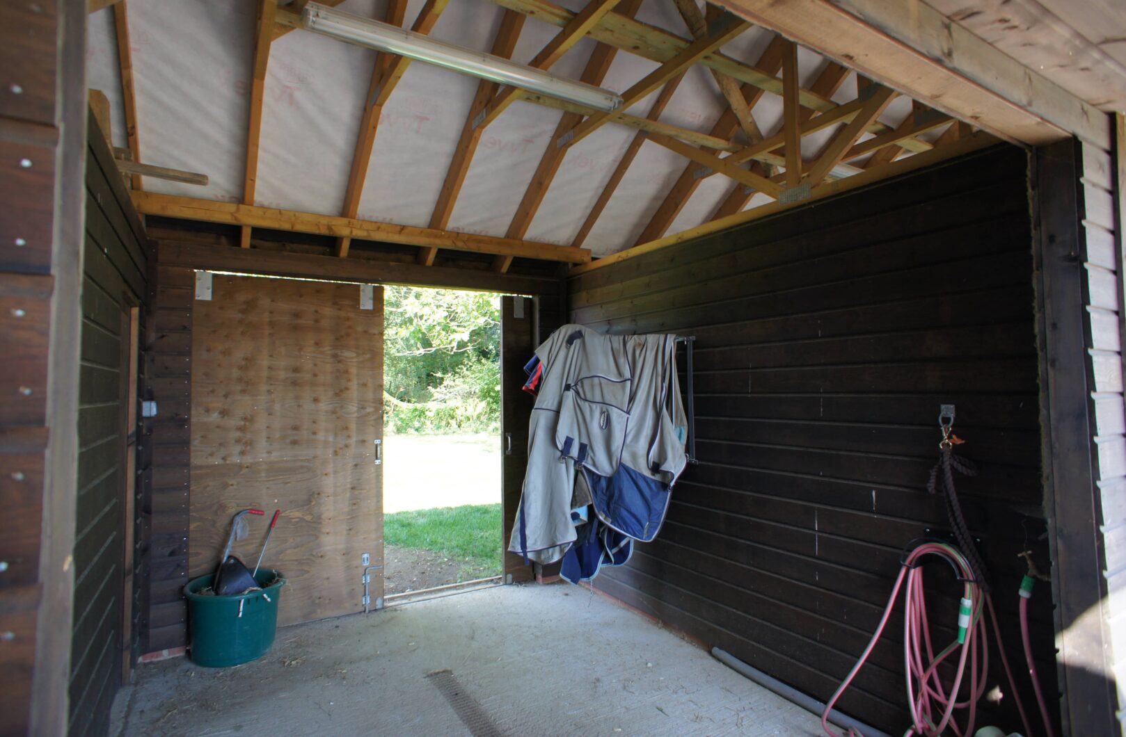 Inside L-shape stable block with clay tiles showing tack hanging up and multi-truss