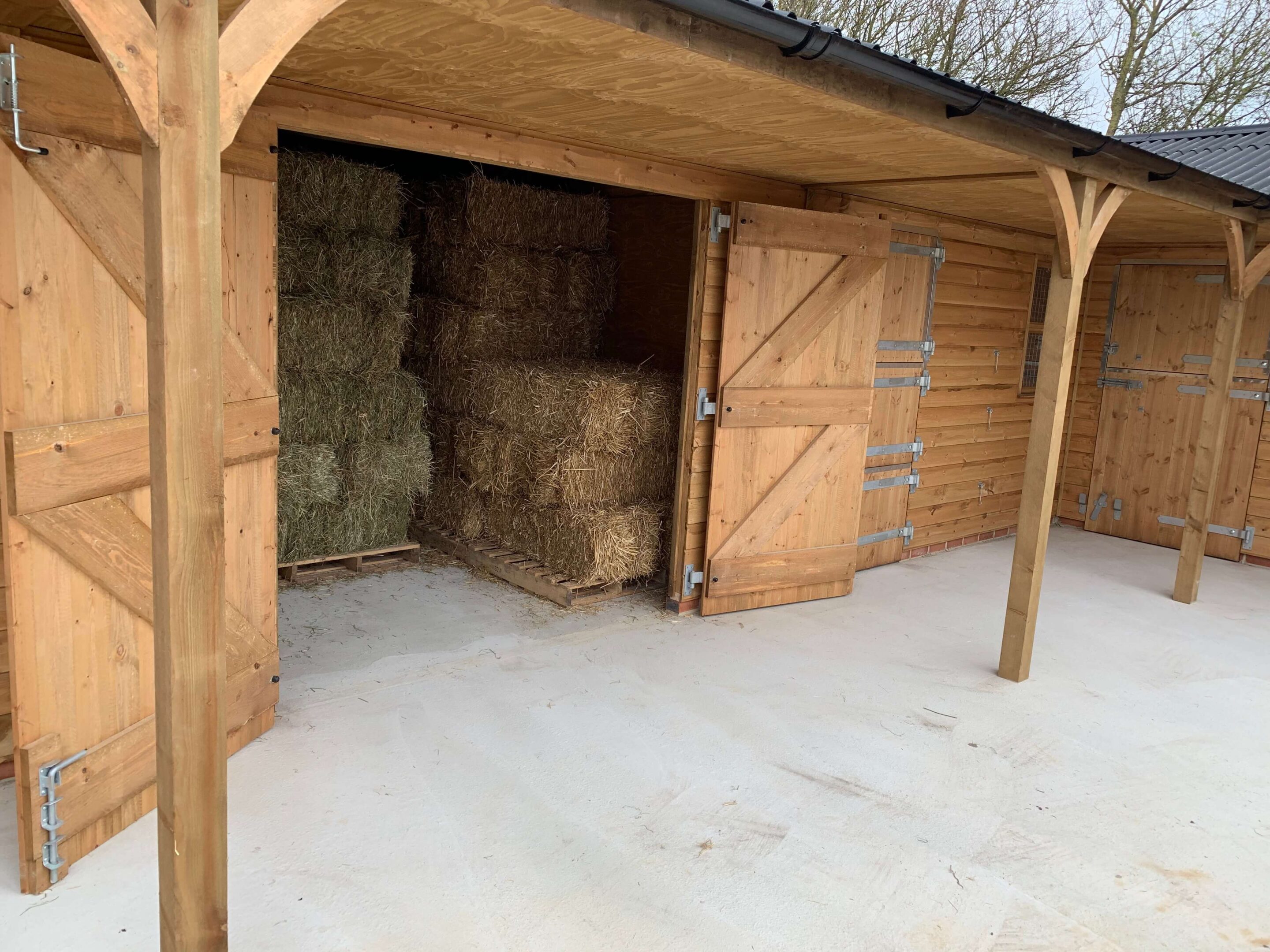 Hay in hay barn, support posts and curved angle braces support the overhang in the foreground