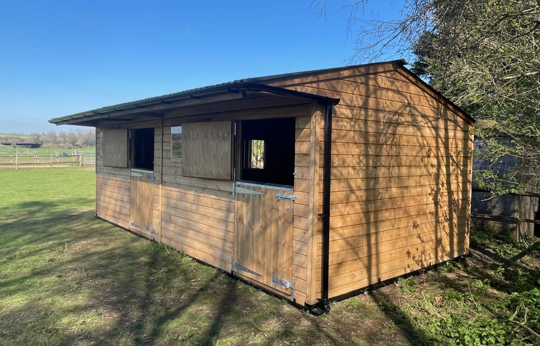 Double mobile stable with top doors open, situated at the side of a low grass paddock