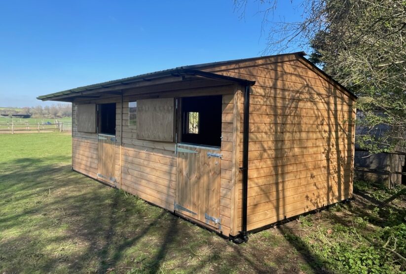 Double mobile stable with top doors open, situated at the side of a low grass paddock