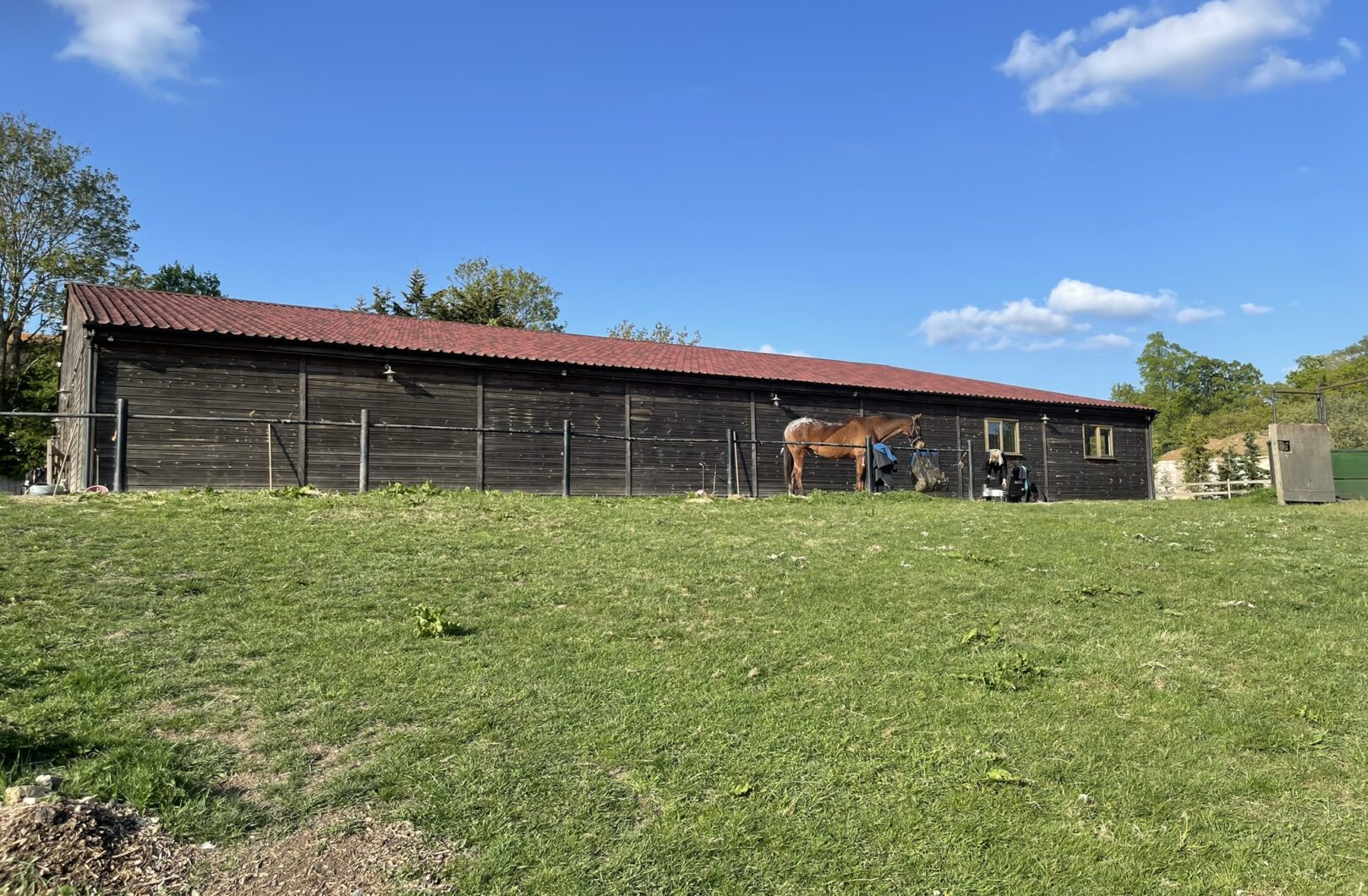 Large american barn with Red Onduline roofing, with horse being washed out front