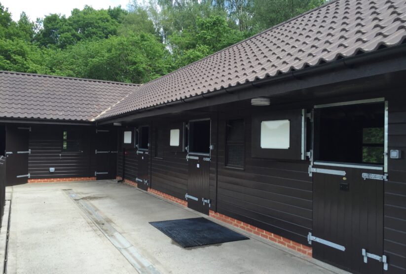 Black stable block with clay tiles, showing stables with top doors open