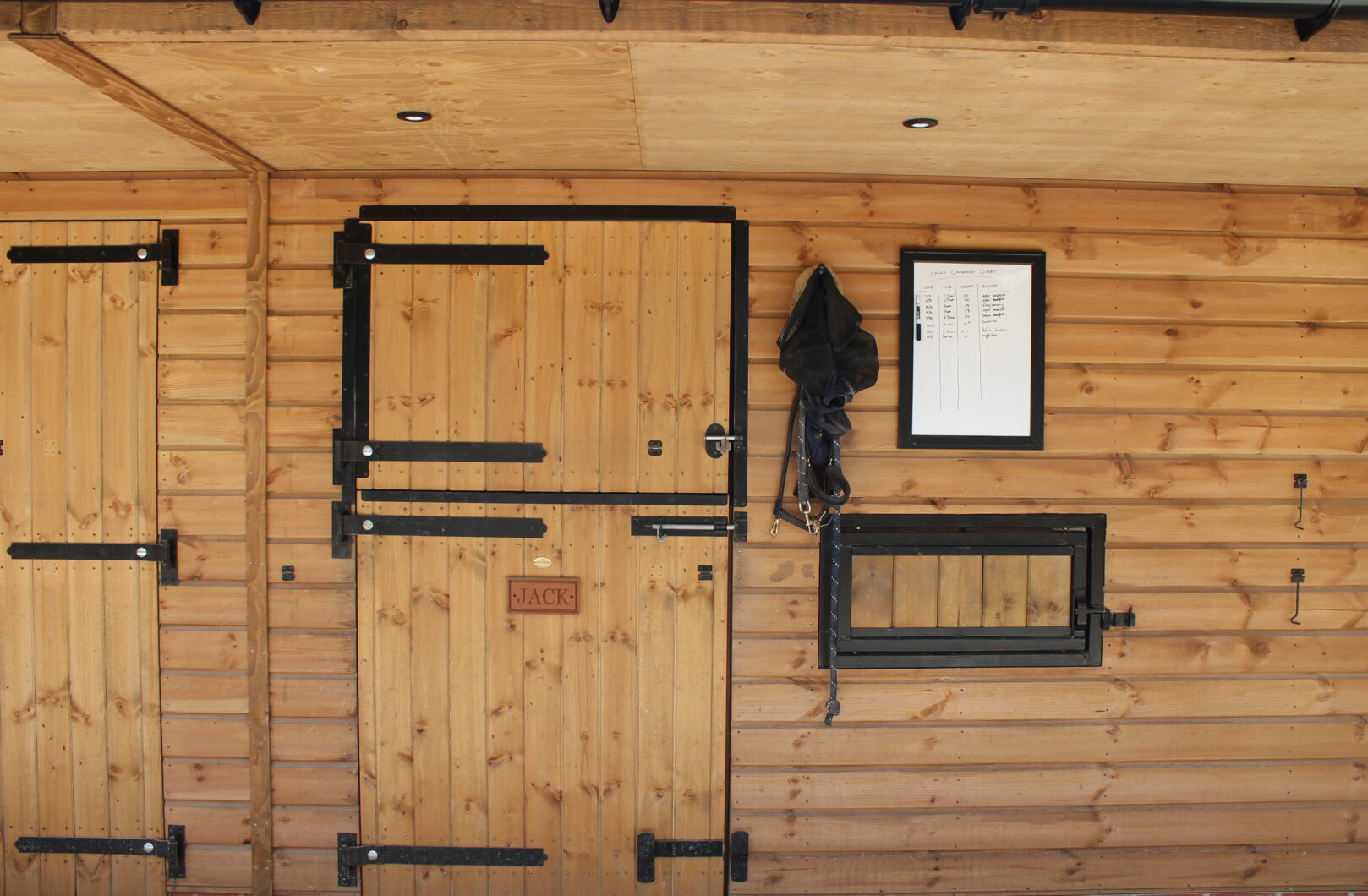 Close up of stable front with whiteboard, tack and black ironmongery